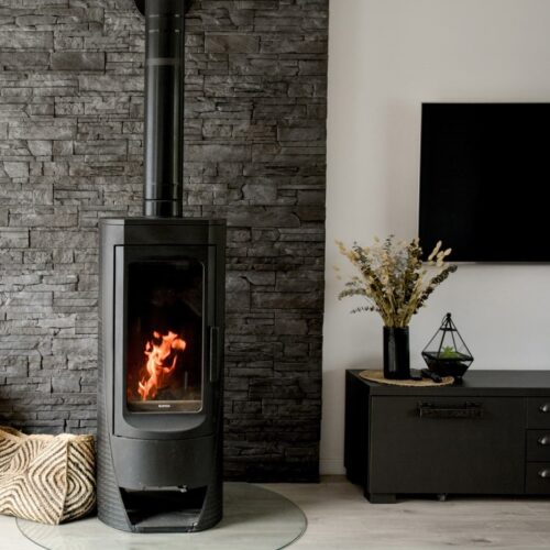 Plamen Nera cast iron wood burning fireplace with large glass door and modern cylindrical design.